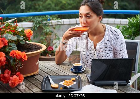Young woman working remotely on her laptop while enjoying a refreshing drink and snack outdoors on a summer day Stock Photo