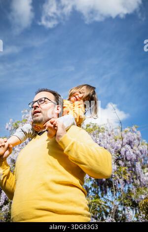 Child sitting on father shoulders looking at camera smiling Stock Photo