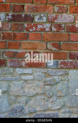 abstract of red brick wall adjoining a stone wall with different building materials being used, New red brick wall on top of old stone wall Stock Photo