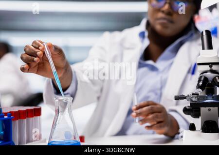 Close up of quality control analyst pipetting agent into blue test tube sample to improve chemical formulation. Research facility expert observing reaction in test tube to verify scientific hypothesis Stock Photo