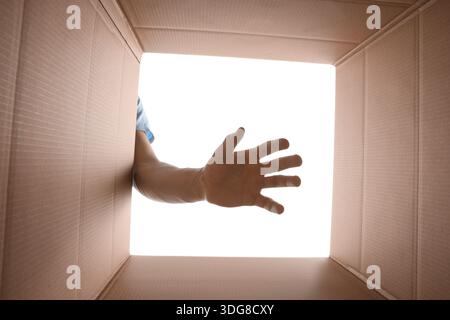 Man reaching into cardboard box against white background, closeup. View from inside package Stock Photo