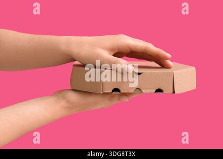 Female hands with takeaway cardboard pizza box on pink background Stock Photo