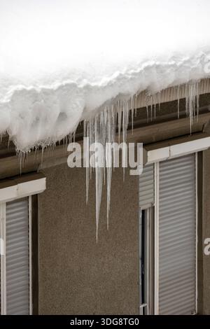 Dangerous sharp icicles on edge of street building roof covered with snow Stock Photo