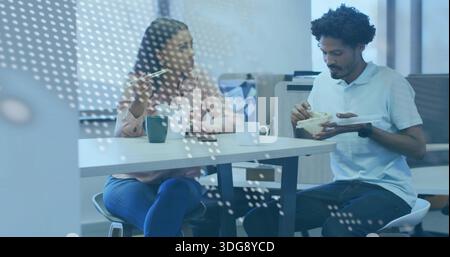 Eating two coworkers in business clothes, sitting in office kitchen with takeout and dotted glass Stock Photo