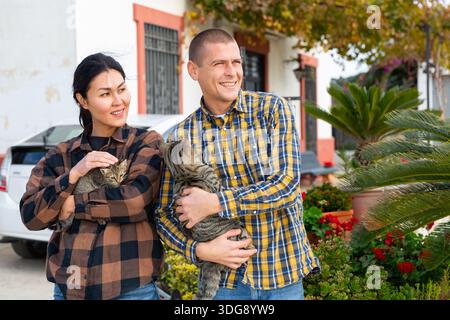 Smiling couple standing with cats near home Stock Photo