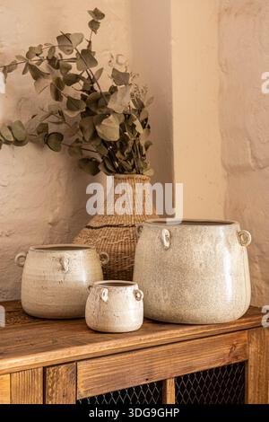 A serene interior decor scene featuring three handcrafted cream ceramic pots with side handles, arranged on a wooden table. Stock Photo