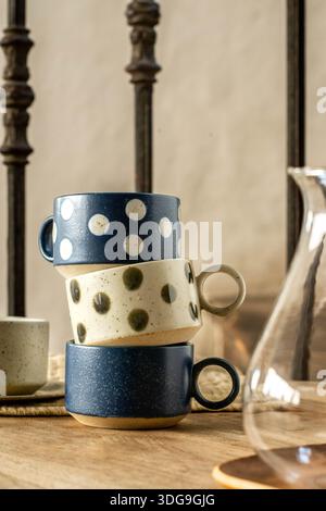 A stack of three artisanal ceramic mugs featuring a charming polka dot design in navy blue and cream white, placed on a wooden surface. Stock Photo