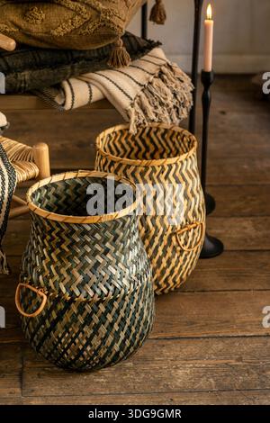 Two tall artisanal woven baskets with a green and natural chevron pattern, styled in a warm rustic room with a wooden floor and a fringed blanket. Stock Photo