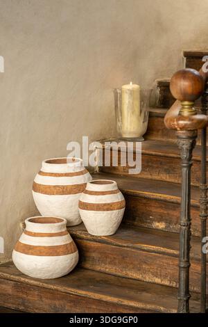 Three handcrafted clay vases with white horizontal stripes arranged on a wooden ledge in a rustic interior setting. Stock Photo