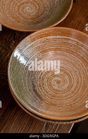A trio of handcrafted terracotta ceramic bowls featuring a white spiral glaze, displayed on a wooden surface in a rustic interior. Stock Photo
