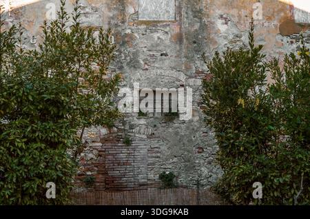 Rustic weathered stone wall with iron window and exposed brickwork in historic Tuscan building. Stock Photo