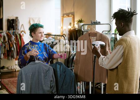 Young Caucasian Woman and Black Man Sorting Second Hand Clothing in Store Stock Photo
