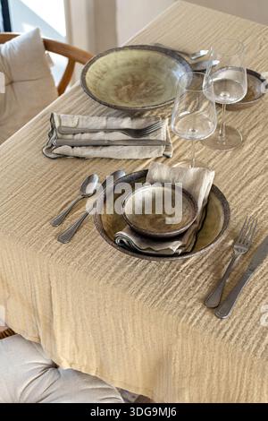 A high-angle shot of a sophisticated table arrangement featuring handcrafted ceramic bowls and plates, silver cutlery, linen napkins, and empty wine g Stock Photo