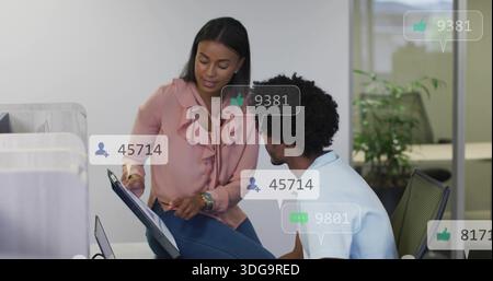 Pointing woman in pink blouse and man in white polo studying tablet at office with overlays Stock Photo