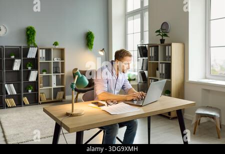 Workaholic man working late with laptop on online project at office desk in night Stock Photo