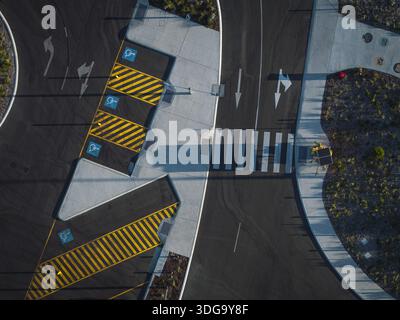 Aerial view of crisp white pedestrian lines cutting through the dark asphalt, contrasting with the yellow striped parking zones and blue disability sy Stock Photo
