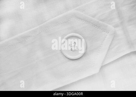 White clothes button sewn on white blank cotton fabric closeup Stock Photo