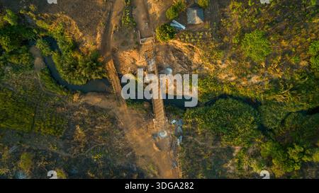 Aerial view of a damaged bridge cutting through a verdant landscape, contrasting with the muddy riverbanks and lush vegetation, Derre, Zambezia Provin Stock Photo