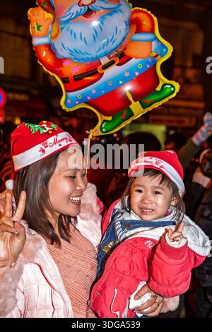 Vietnamese mother and daughter together enjoying Christmas night outdoor party at St. Joseph's Cathedral, Old Quarter, Hanoi, Vietnam Stock Photo