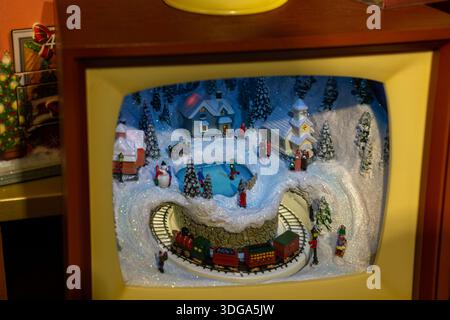 Detailed Christmas miniature scene showing a snowy village with small houses, figurines, and a toy train circling the display. Stock Photo