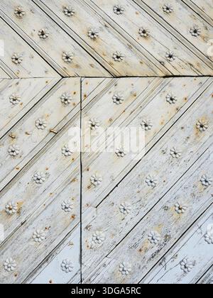 Weathered white wooden door with diagonal planks, rust stains and decorative rosettes. Suitable for background and text areas. Copyspace Stock Photo