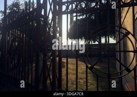 Path that leads to a protective fence in a park at sunset seen through a gate Stock Photo