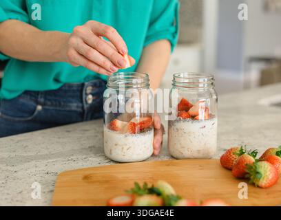 Woman Pouring out Chia Seeds into Overnight Oats Stock Photo