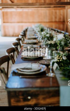rustic table set for dinner with flower arrangements in a barn Stock Photo