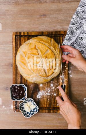 Hands cutting loaf of sourdough bread on cutting wooden board Stock Photo