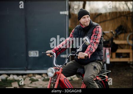 Man rides a red bicycle wearing a black vest and a plaid shirt Stock Photo