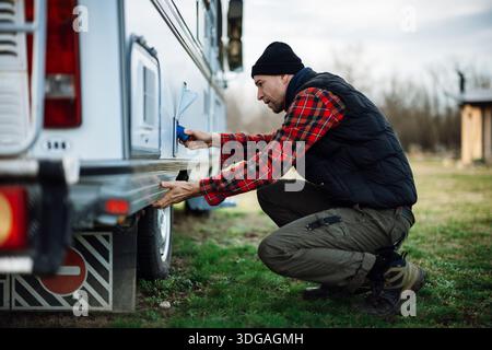 Man working on the side of a camper van in an outdoor setting Stock Photo