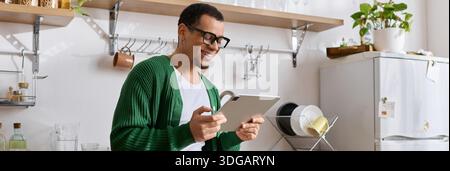 A stylish young man smiles while using a tablet in a warm and inviting kitchen atmosphere. Stock Photo