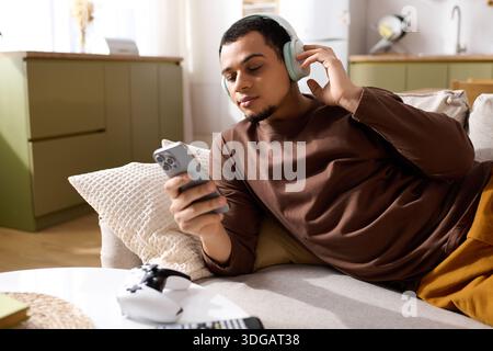 Handsome young man relaxes on the sofa, listening to music while using his phone. Stock Photo