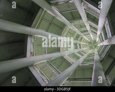 Abstract, low-angle view looking straight up into the core of a modern structure, showing multiple converging white columns and metal grating forming Stock Photo