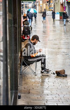 Street musician or busker playing a ukelele on a rainy day in Lincoln City centre, Lincolnshire, England, UK Stock Photo