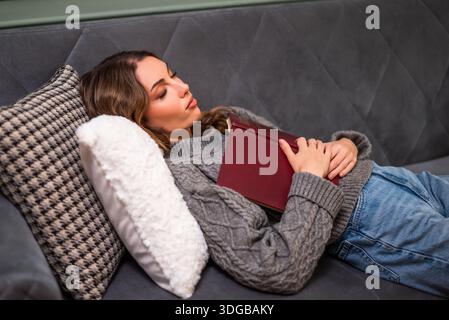 Young woman fell asleep while reading book at home. She is relaxing on her bed. Stock Photo