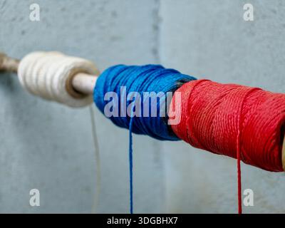 Spools of red, white, and blue thread wound tightly on a wooden rod, forming a textured, striped pattern ideal for textile, sewing, craft, and diy bac Stock Photo