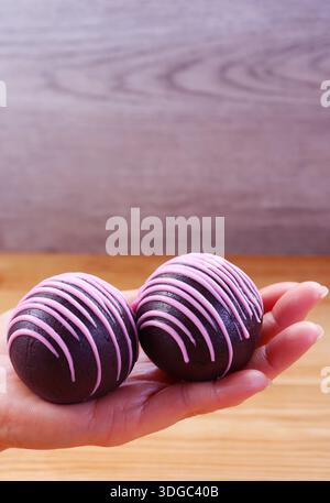 Pair of Chocolate Cake Pops Coated with Strawberry Royal Icing in Hand Stock Photo