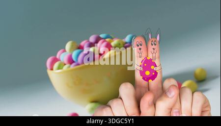 Image of fingers with easter bunny faces and easter eggs on blue background Stock Photo