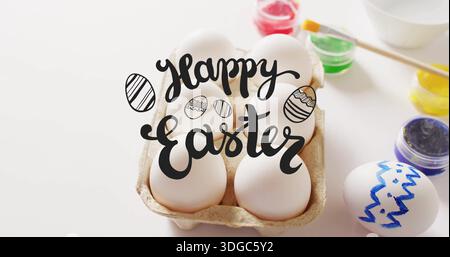 Image of happy easter text over eggs and paints on white background Stock Photo