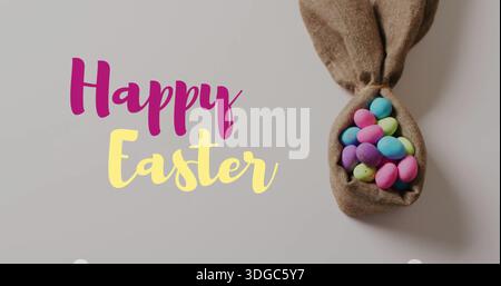 Image of happy easter text over colourful easter eggs in cloth on grey background Stock Photo