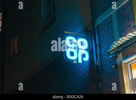 Illuminated Co-op supermarket logo on the exterior of a retail building at night, showing branded signage on a UK high street in an urban setting. Stock Photo