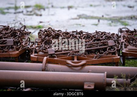 Rusty fishing dredges with heavy chains on the ground in a coastal industrial setting. Weathered fishing dredges and chains - maritime industry. Stock Photo