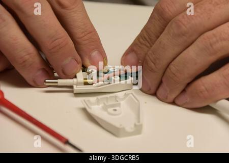 Man's hands working on repairing an electrical plug, connecting wires for home maintenance Stock Photo