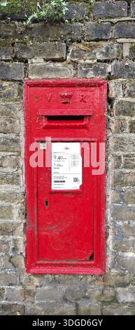 Old red metal mailbox mounted on a weathered brick wall. Evoking urban history, communication heritage and passage of time in a city: London Stock Photo