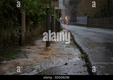 Floodwater rushing along a city street after heavy rainfall, overflowing the sidewalk and drainage system in an urban area. Urban flooding. Stock Photo