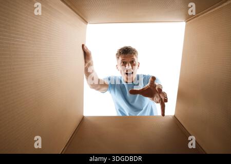 Man looking into cardboard box against white background, view from inside package Stock Photo