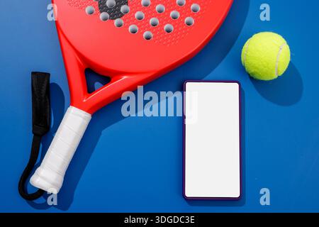 Flat lay of padel racket and ball with blank smartphone screen on blue court for club app reservation and promotion Stock Photo