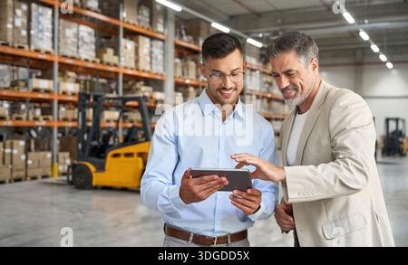 Warehouse managers team standing near cardboard boxes using tablet. Stock Photo