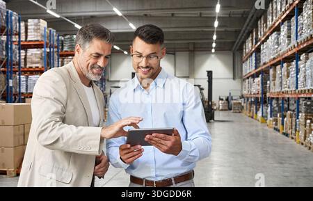 Warehouse managers team standing near cardboard boxes using tablet. Stock Photo